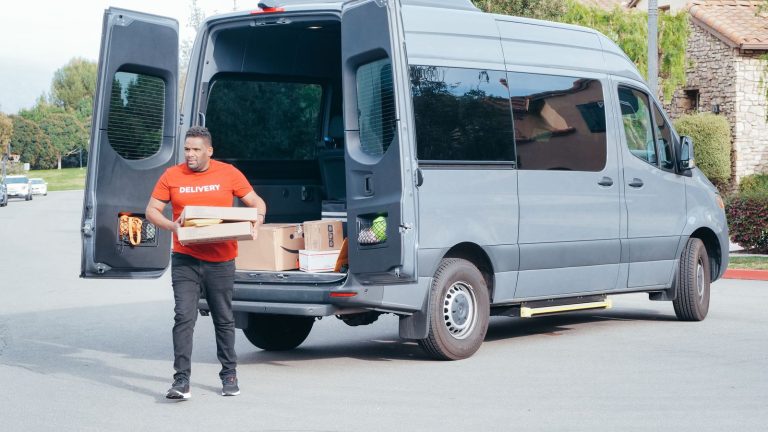 Mitarbeiter entlädt Kartons aus einem Transporter vor einem Geschäftsgebäude