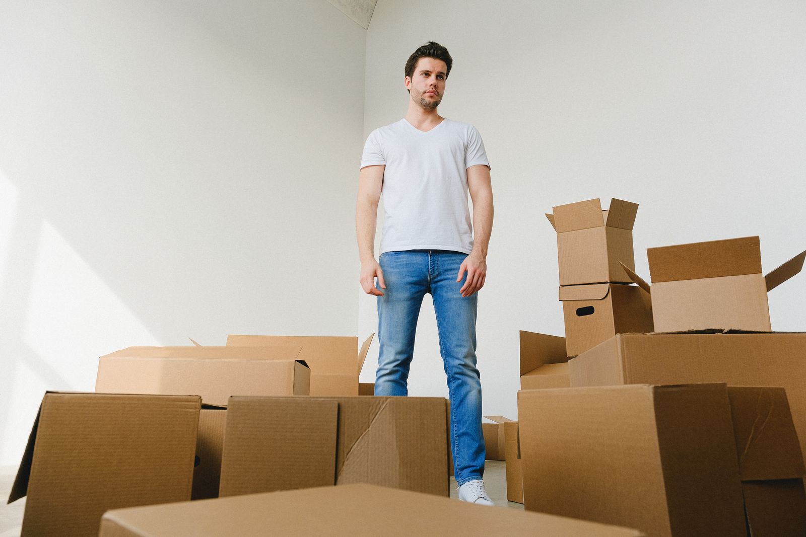 Mann steht zwischen gepackten Umzugskartons in einer leergeräumten Wohnung